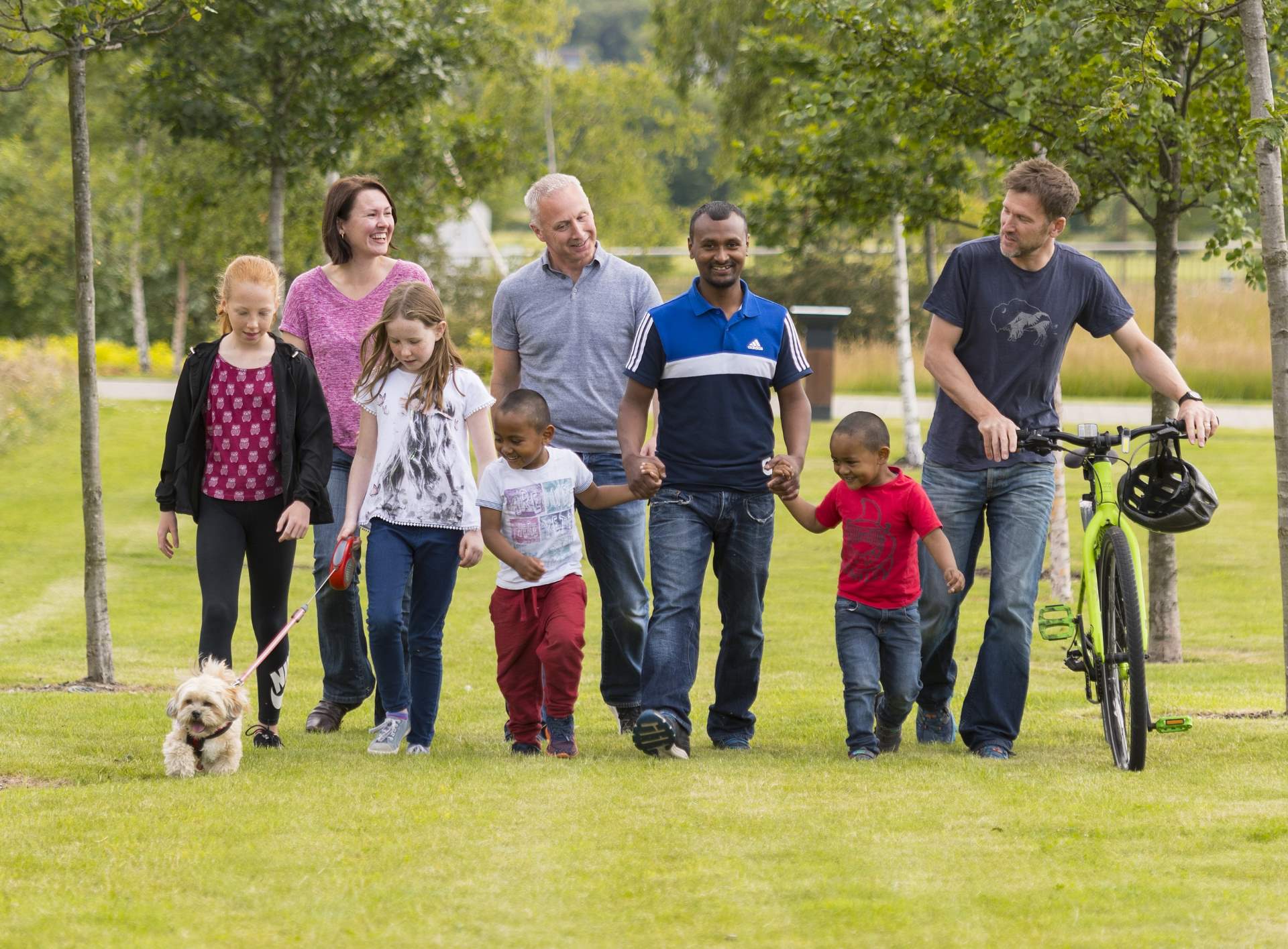 Group of people, including children and dogs walking through a park