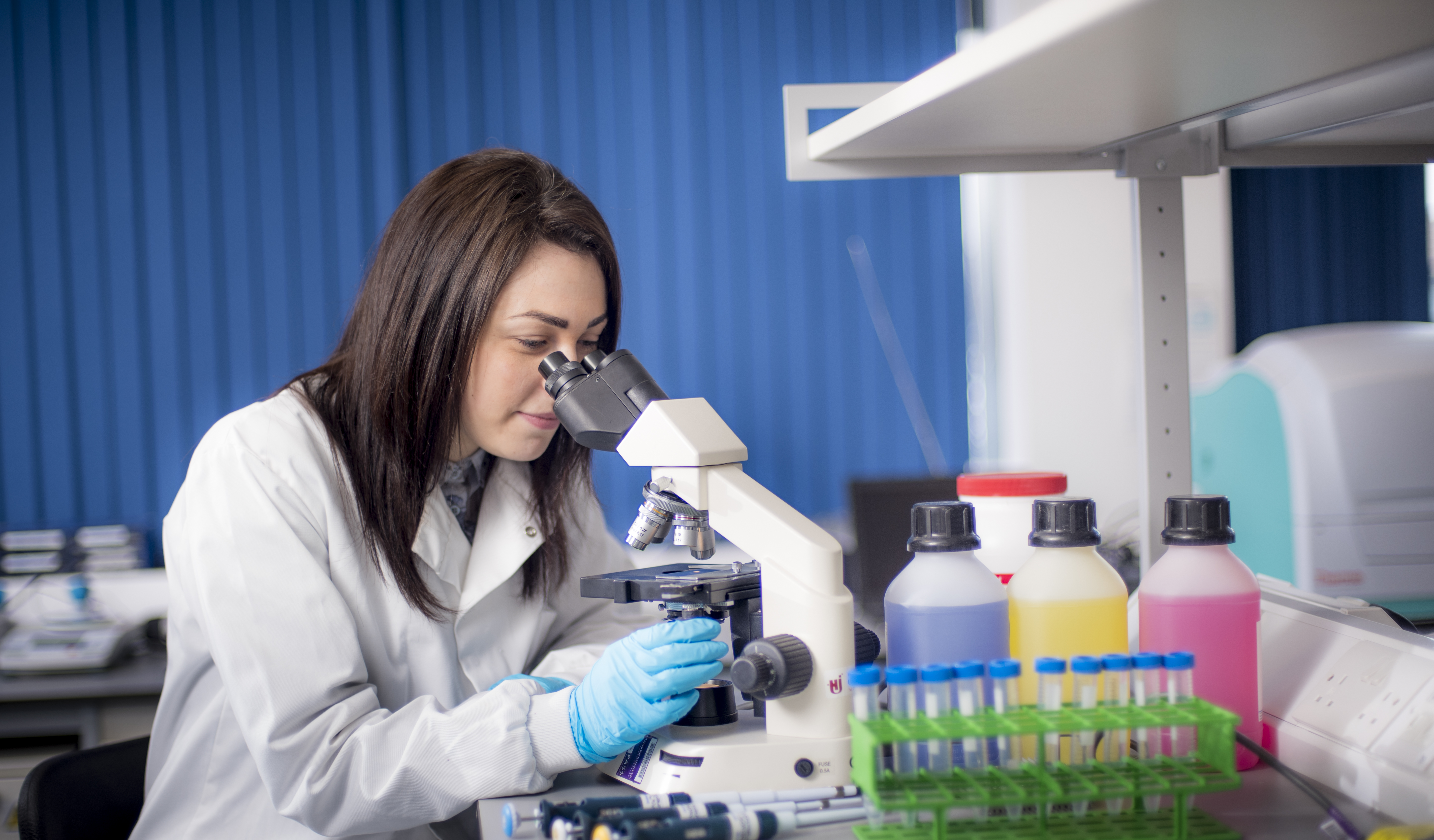 Young woman in white coat looking into microscope