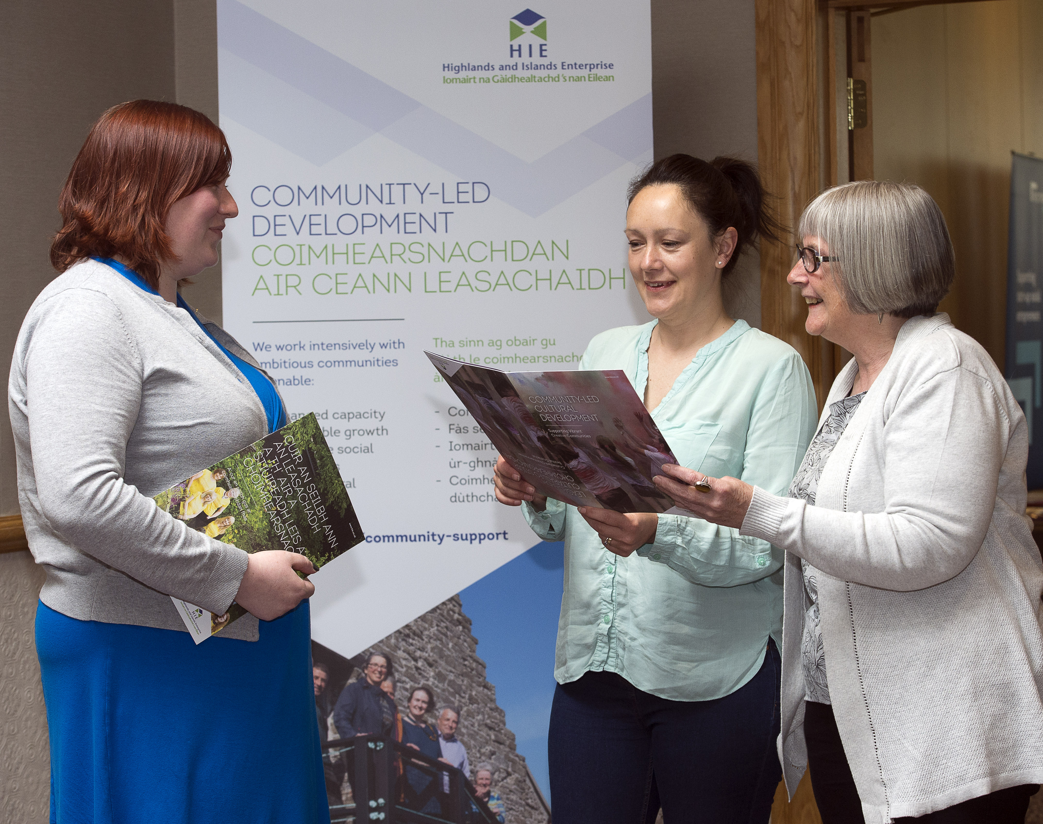 three women at a HIE exhibition stand about community development